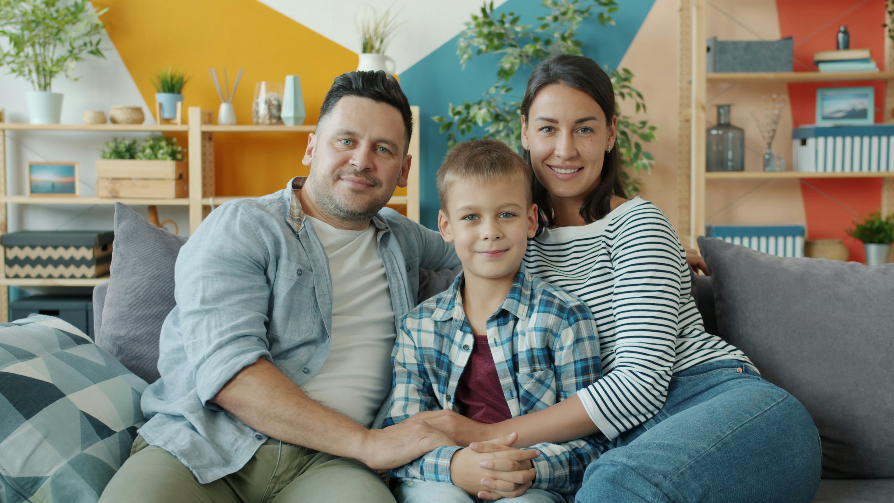 Pai, mãe e filho abraçados no sofá da sala